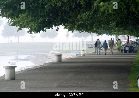 View along the promenade at the side of the Somme estuary with group of people enjoying afternoon stroll at St Valery sur Somme Stock Photo