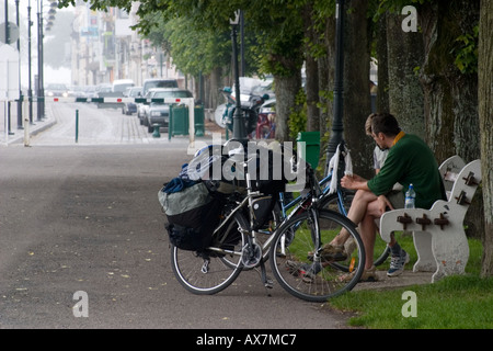 Couple of cyclists take a break and rest on a bench on the riverside promenade in St Valery sur Somme Stock Photo
