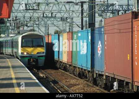 Stratford interchange station with One Great Eastern passenger train beside container train Stock Photo