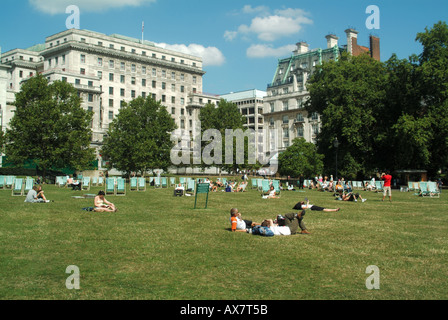 London Green Park weekday lunchtime office workers and tourists relaxing in and around deckchairs Stock Photo