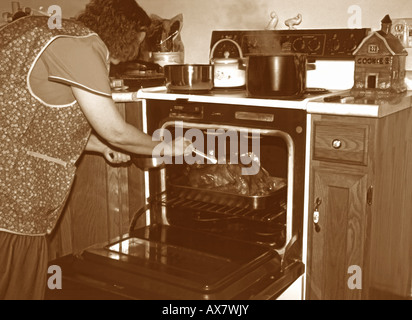 Homemaker basting a golden brown turkey, as she cooks dinner on Thanksgiving day for her family, that will soon arrive. Stock Photo