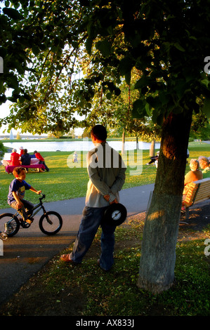 A man watches his son play on a bicycle in a park Stock Photo