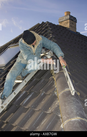 builder with spirit level fitting ridge tiles to a roof of a new home Stock Photo