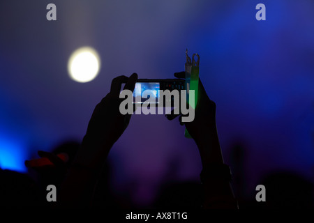 hands in the air in the crowd taking video with a mobile phone and holding a glowstick at a dance event in Belfast Northern Irel Stock Photo
