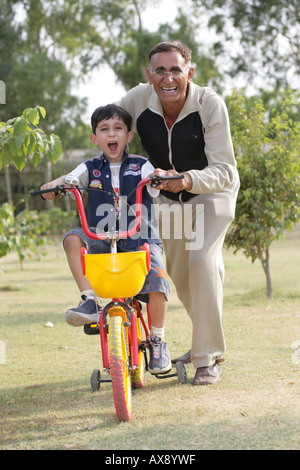 Portrait of a boy learning bicycle with the help of his grandfather in a park Stock Photo