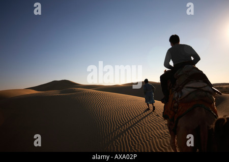 A late afternoon silhouette of a guide leading a camel and passenger over sand dunes. Stock Photo