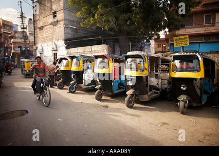 Two young boys ride on a single bicycle past a row of auto-rickshaws in Jodhpur, Rajasthan, India. Stock Photo