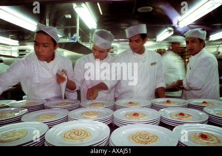 A team of Filipino chefs plating dishes in a large-scale catering kitchen of cruise ship Stock Photo
