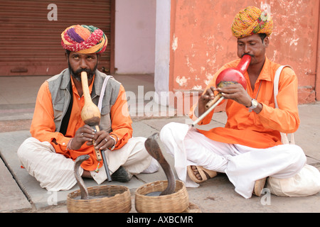 A snake charmers in the Jaipur, India. A man in an orange shirt and turban is playing a pipe, two cobra snakes rising out. Stock Photo