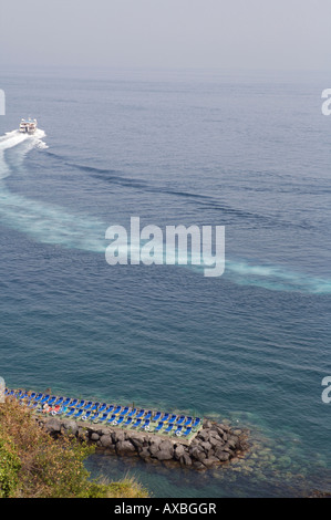 The Capri Ferry sets sail to Capri in the morning arcing out of the port of Sorrento with blue sun chairs in the foreground Stock Photo