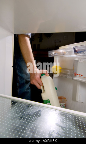 View from inside a fridge as a man takes two pints of semi skimmed milk from the door. Stock Photo