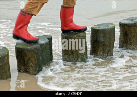 MR legs in rubber boots walking on a protection barrier made of wodden blocks at the coast of Baltic Sea by Heringsdorf Stock Photo