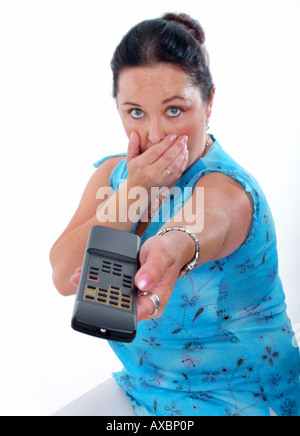 astonished woman points with remote control, with her hand on mouth Stock Photo
