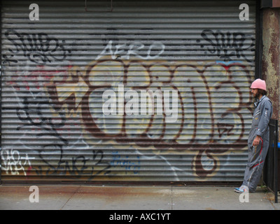 young worker smoking a cigarette next to a metal grate with graffiti, USA, Brooklyn, New York Stock Photo