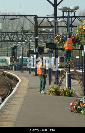 Shenfield railway station workmen putting hanging baskets onto lamp posts on platform using step ladder Stock Photo