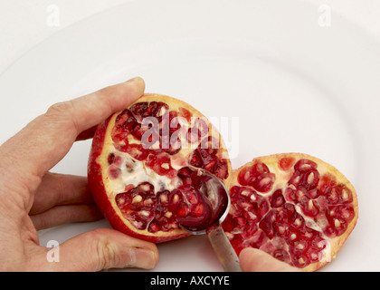 man eating seeds from a sliced pomegranate on a white plate Stock Photo