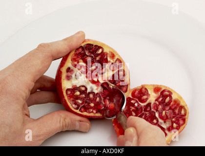 man eating seeds from a sliced pomegranate on a white plate Stock Photo