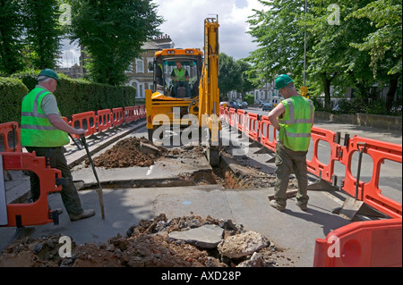 Excavating trench behind traffic barrier in preparation for   installing replacement polyethylene water pipe in an inner city. Stock Photo