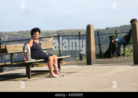 Old lady with walking stick resting on a cliff top seat on the North Bay at Scarborough, Yorkshire. Stock Photo