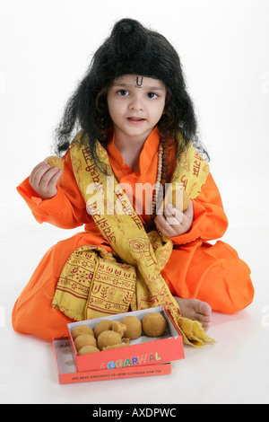 Portrait of a boy in priest clothing eating laddu Stock Photo