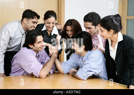 Two businessman arms wrestling with their colleagues watching them in a office Stock Photo