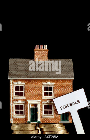 a house for sale sunk in debt balancing on a stack of british pound coins struggling under the recession Stock Photo