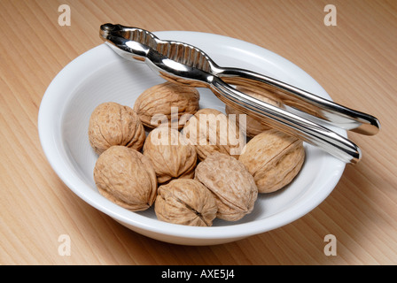 A bowl of walnuts and a nutcracker standing on a wooden table Stock Photo