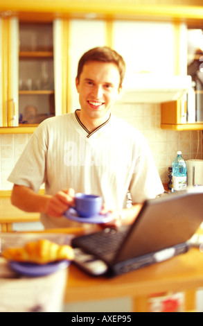 Young man drinking from a cup while using a computer. Stock Photo