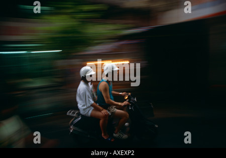 A Chinese couple speed past on a scooter in the Chinese Special Administrative region of Macau. Stock Photo