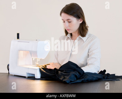 A young woman using a sewing machine to stitch a dress. Stock Photo