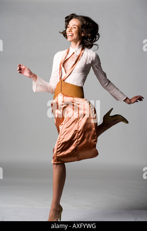 young woman in the studio jumping wearing a orange skirt white blouse and high heels Stock Photo