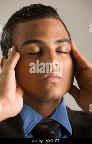 Young man with his eyes closed and hands to his temples - perhaps he has a headache Stock Photo