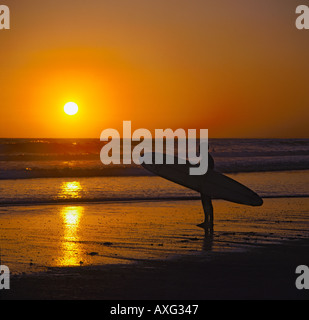 A single Surfer standing with his surfboard silhouetted against sunset in the wet sands at St Ouen Bay Jersey Channel Islands Stock Photo