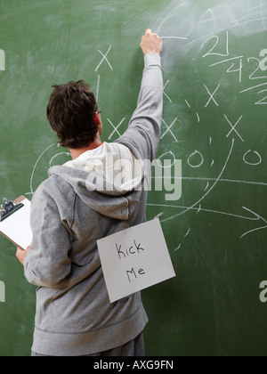 Man at Blackboard with Kick Me Sign on Back Stock Photo