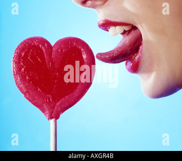 Young woman licking a heart shaped lollipop.