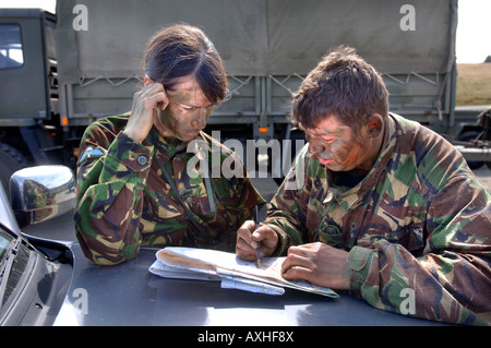 A BRITISH ARMY FEMALE RECRUIT CHECKS A MAP WHILE BEING BRIEFED BY A COLOUR SERGEANT BEFORE A TRAINING STALK DURING A SNIPER COUR
