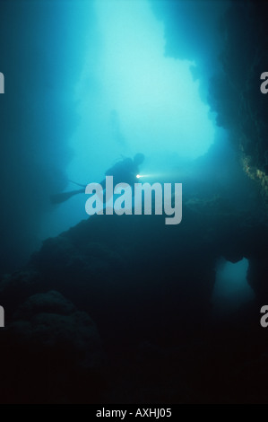 scuba diver shines a light on rock formation in a cave Stock Photo