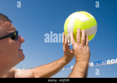 A volleyball player lobs a ball during a game at the beach Stock Photo