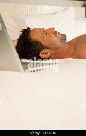 Young unshaven man lying on a bed behind a laptop, selective focus Stock Photo