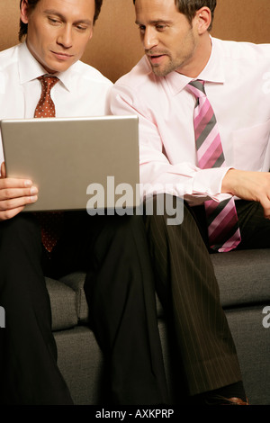 Two businessmen using laptop, sitting on a sofa Stock Photo