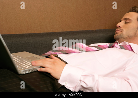 Businessman sleeping on a sofa, laptop at his lap Stock Photo