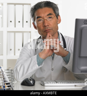 Senior male doctor sitting at computer Stock Photo