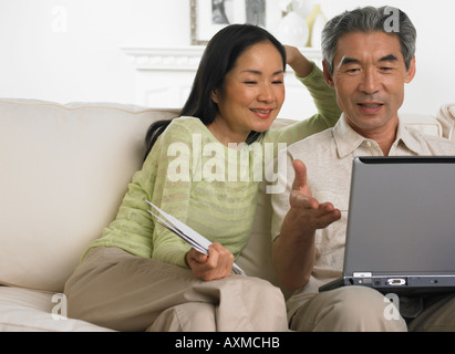 Middle aged Asian couple sitting on sofa with laptop Stock Photo
