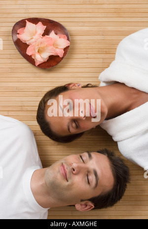 Couple laying on floor with eyes closed next to flowers Stock Photo