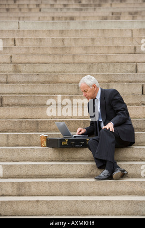 Man sitting outdoors on stairs with laptop Stock Photo