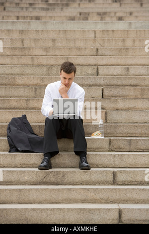 Man sitting outdoors on stairs with laptop Stock Photo