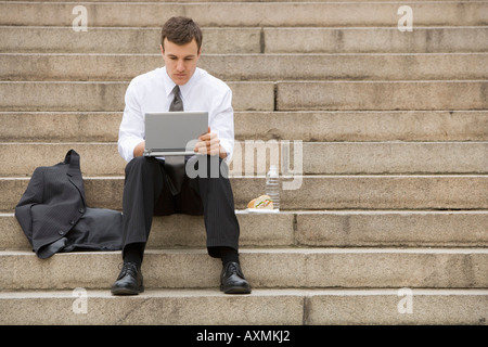 Young adult male sitting outdoors on stairs with laptop Stock Photo