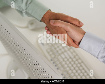 Two men shaking hands over computer Stock Photo