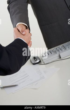 Businessmen shaking hands over computer Stock Photo