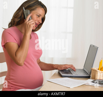 Pregnant woman using telephone and laptop Stock Photo